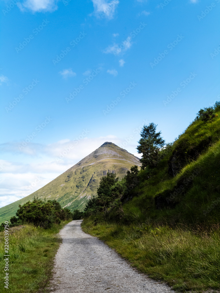 Obraz premium Gravel path leading toward a conical peak in the Scottish Highlands