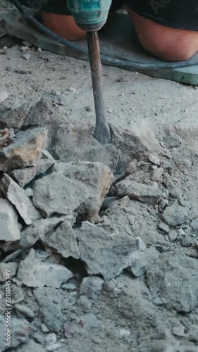 close ground-level view of rotary hammer chisel driven into concrete floor, sending dust plume and rubble.
