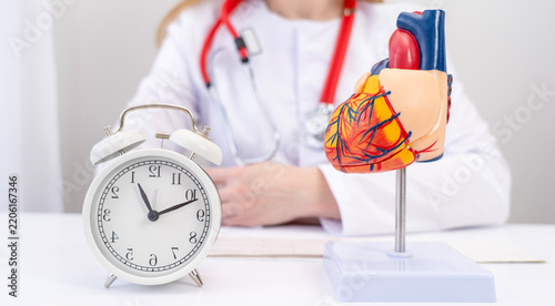 Doctor sits calmly beside heart model and clock