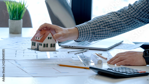 Hand holds miniature house model above blueprints