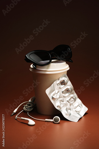 Black sunglasses on top of a coffee cup, earbuds and blister pack