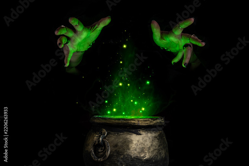 Witch's hands over a cauldron with a magic potion in a dark room. Witch casting spells on Halloween night