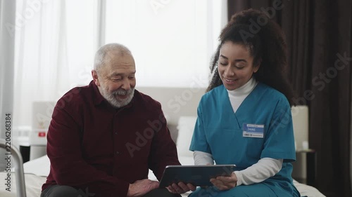 African American nurse helping elderly man install banking app on tablet