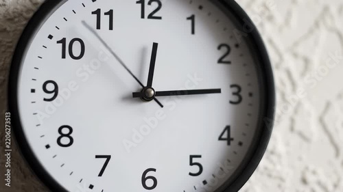 Clock hanging on textured white wall with moving second hand showing time passing