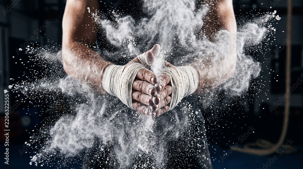 Fototapeta premium Close up of athlete hands clapping together with white chalk powder explosion in dark gym setting. Fitness training, bodybuilding, strength and conditioning.