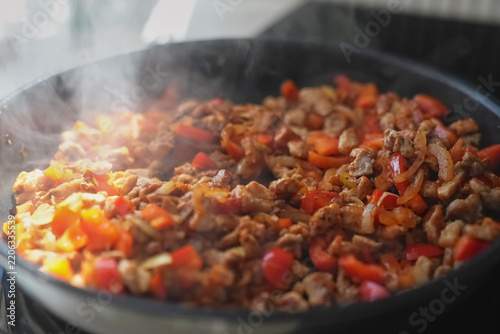 Meat pieces with red pepper and onion cooking in hot frying pan with steam rising