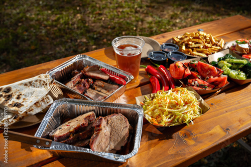 Delicious barbecue feast featuring smoked meats, fresh vegetables, and refreshing drinks in a sunny outdoor setting