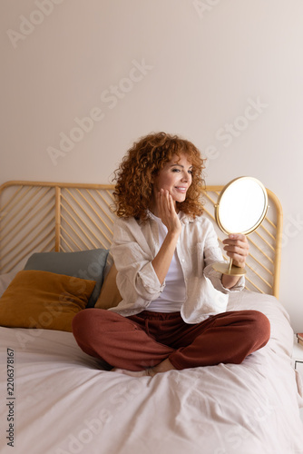 Woman checking skincare routine in bedroom mirror