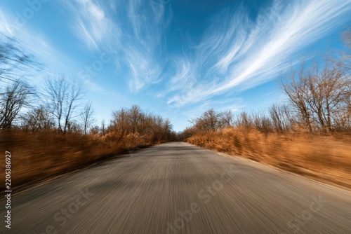 Streaking asphalt road through autumn woods under wispy blue sky