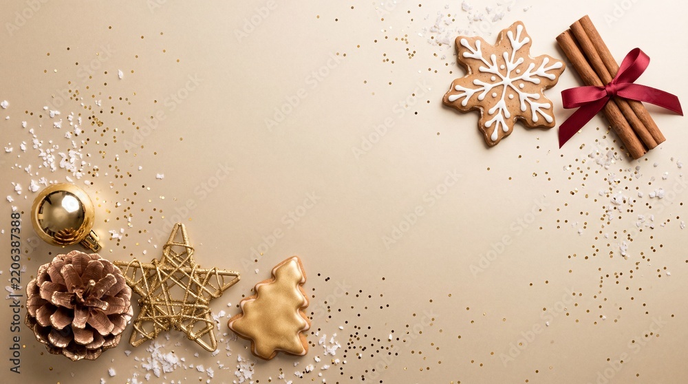 Obraz premium Elegant Christmas and New Year festive background with golden ornaments, gingerbread cookies, cinnamon sticks, and glitter on beige surface with central copy space for text.