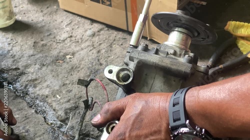 technician is assembling pieces of a broken car air conditioning compressor on the pavement.