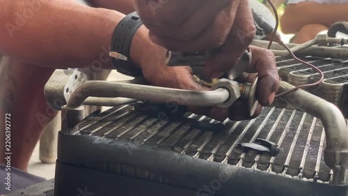 technician is assembling pieces of a broken car air conditioning evaporator on the pavement.