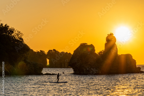 Golden Hour Sunset View of Rocky Coastline and Kayaking Activity. Dramatic tropical seascape.