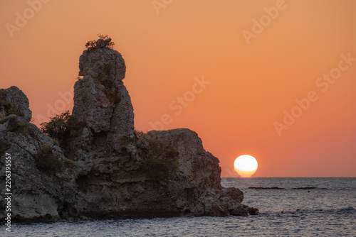 Sunset over rugged coastal rocks and dramatic sea stacks, capturing the warm gradient of twilight sky.