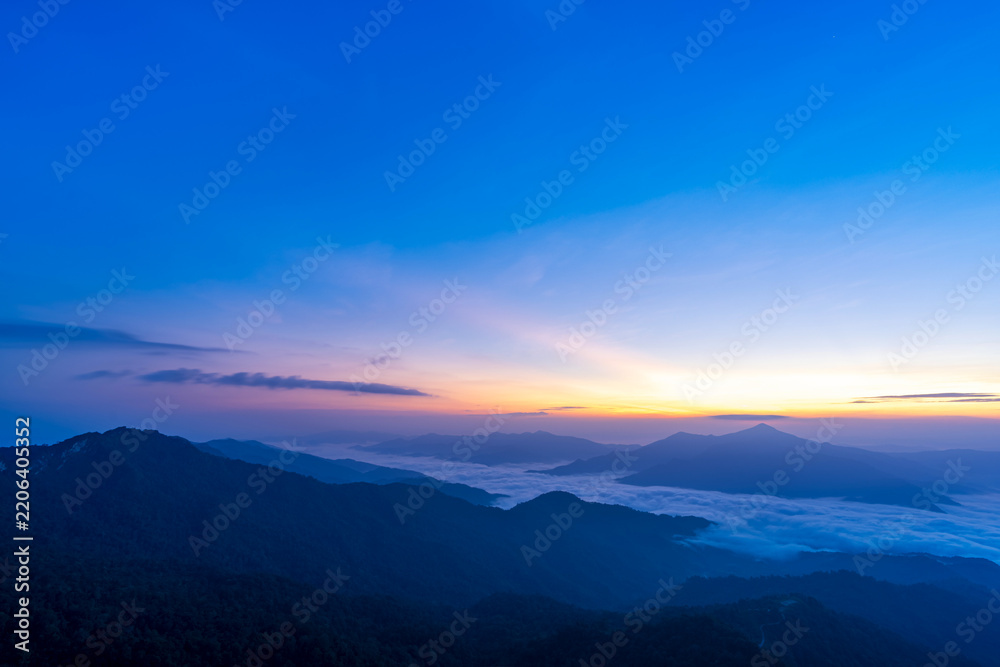 Fototapeta premium Blue hour sky above layered mountains and a sea of clouds with colorful sunrise and sunset glow