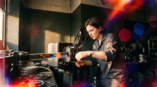 Female Projectionist Threading Vintage Analog 35mm Movie Film Reel into Projector in Dark Cinema Booth