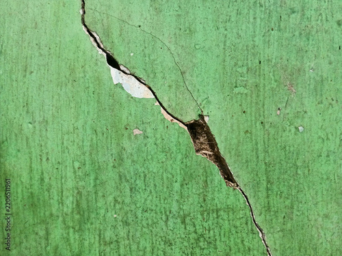Deep diagonal crack on damaged green concrete wall texture background