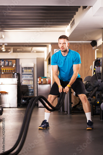 Man exercising with battle ropes in a gym setting during the day