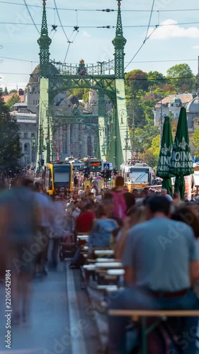 Budapest Liberty Bridge time lapse with vibrant street food festival crowd, yellow tram, and historical architecture under sunny sky
