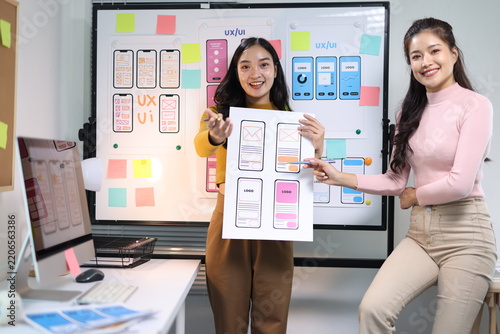 Young woman developer presenting UX/UI mobile app design wireframes to a colleague, discussing layout and prototyping ideas.