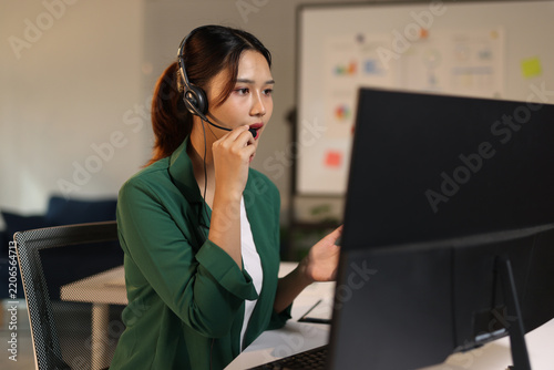 Asian woman call center agent or customer service representative working with a headset and computer in office.