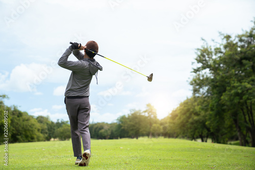 Golfer completing swing follow through with driver on green course