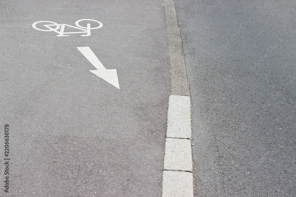 Fototapeta premium Bicycle lane marking on asphalt road with directional arrow indicating bike path, concrete curb visible along the edge of the lane