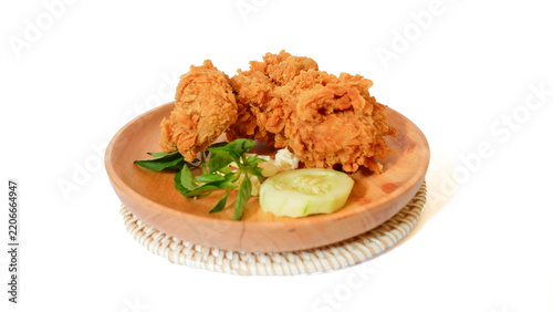 Tasty crispy breaded golden fried chicken pieces served on a wooden plate with fresh cucumber and basil garnish, isolated on a white background for menu and advertisement.
