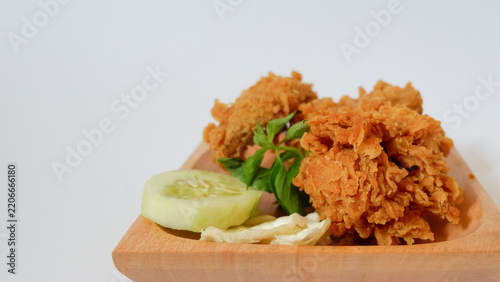 Crispy golden fried chicken served on a wooden plate with fresh cucumber and cabbage garnish, delicious crunchy breaded poultry for restaurant food menu on white background.