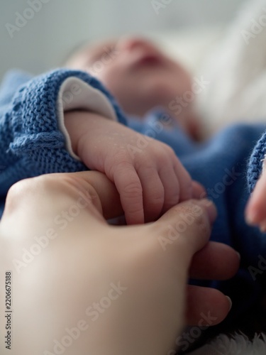 Newborn Baby Hand Holding Parent Finger Infant Bonding Family Love Care Touch.  Close-up of a newborn baby gently holding a parent’s finger while resting in soft blue clothing. 