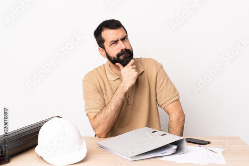 Caucasian architect man with beard in a table having doubts.