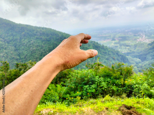 Fotografie POV hand reaching for green mountain valley landscape