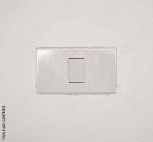 Simple white plastic light switch panel mounted on a white concrete wall