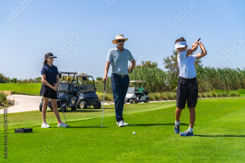 Golf instructor teaching children swinging golf clubs on course