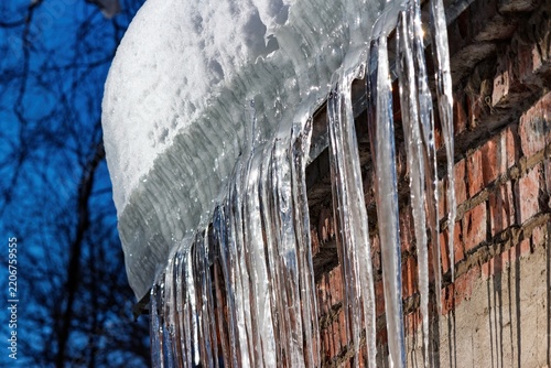 Foto Glistening sharp icicles dangle from a snow-covered roof edge against a rustic brick wall, sparkling under winter sun
