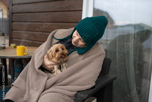 Adult man in a warm knit blanket and knitted hat on a home terrace sipping a hot drink