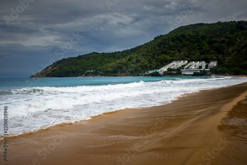 Tropical secluded beach with golden sand, scenic green hill and ocean waves under blue sky