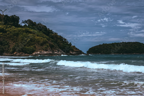 Tropical secluded beach with golden sand, scenic green hill and ocean waves under blue sky