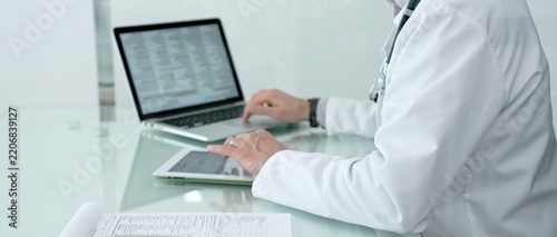 Healthcare professional using a laptop, digital tablet, and medical records, managing patient information and health data in a modern clinic or hospital setting
