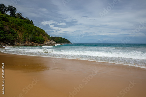 Tropical secluded beach with golden sand, scenic green hill and ocean waves under blue sky