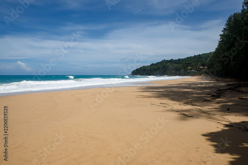 Tropical secluded beach with golden sand, scenic green hill and ocean waves under blue sky