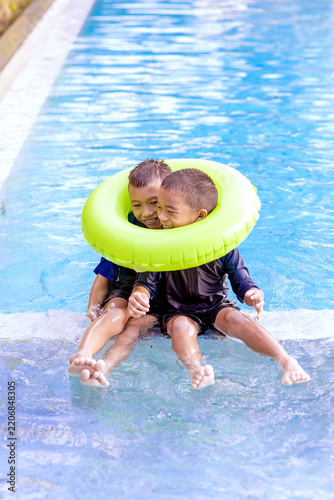 Happy Brothers Having Fun Sharing a Swim Ring in Resort Pool
