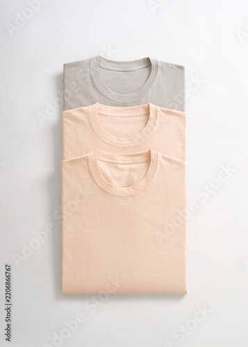 A stack of neatly folded pastel colored cotton t shirts in neutral shades on a white background