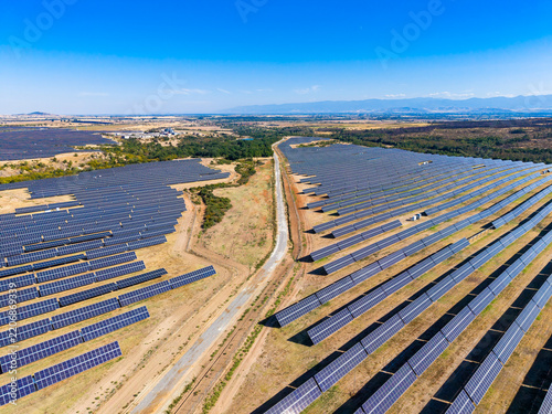Large solar panel farm in an open landscape with multiple rows of panels under clear blue sky