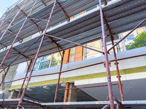 Construction work takes place at a building site with scaffolding set up around the structure in a city setting during daylight hours