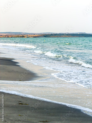 Fotografie Waves gently roll onto the shore in a coastal scene with a distant landform unde