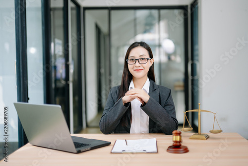 Asian female lawyer in a suit and glasses sitting at her modern office desk. Professional attorney providing trusted legal advice