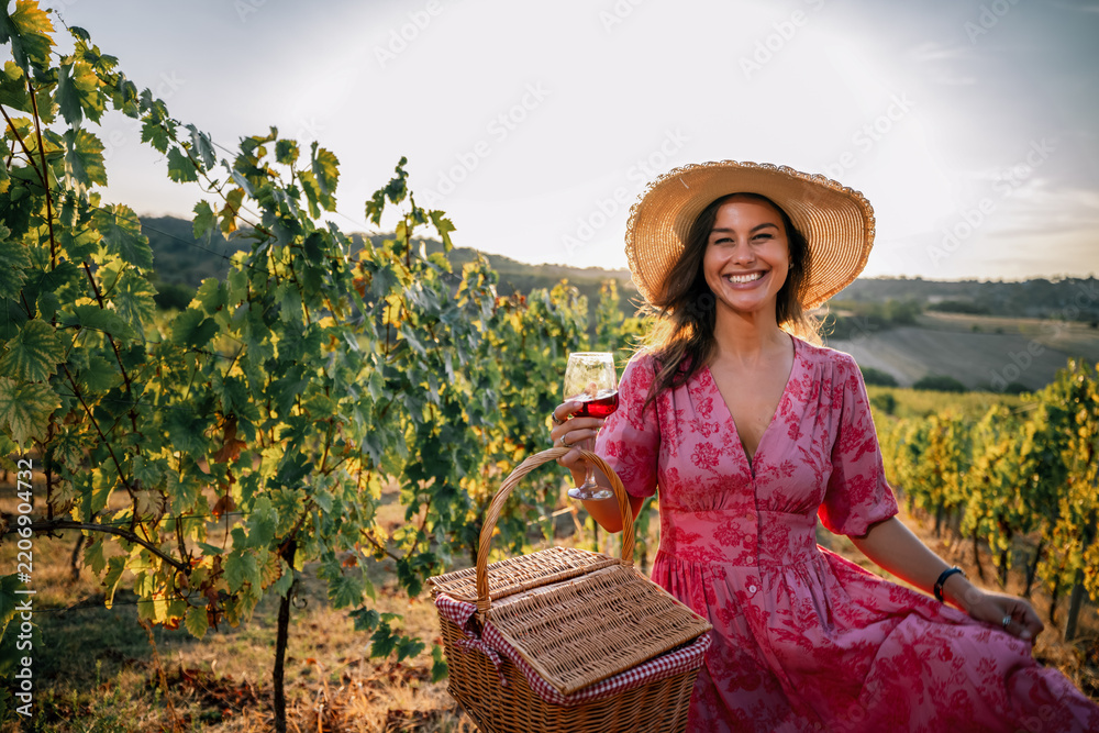 Obraz premium Woman sitting in vineyard with picnic basket and glass of red wine