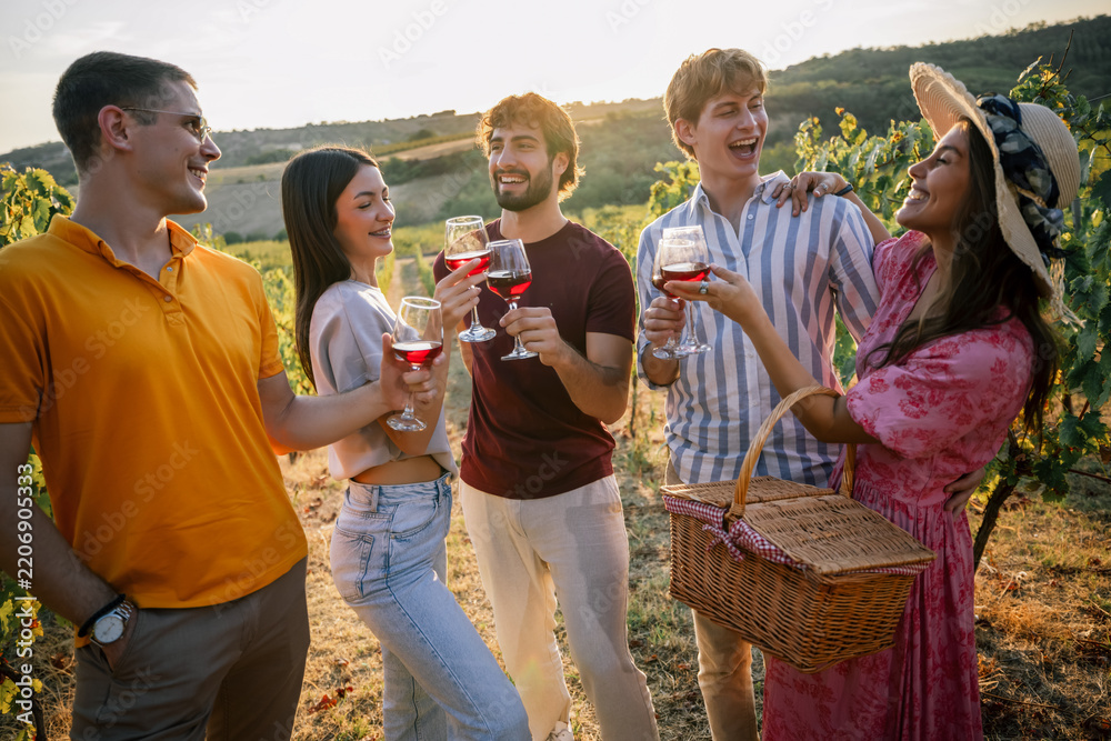 Fototapeta premium Young people enjoying wine tasting together in sunset vineyard row