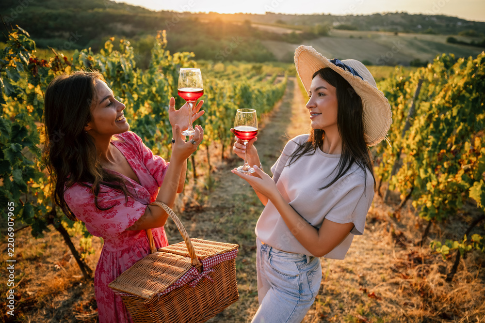 Obraz premium Two female friends inspecting glasses of red wine at vineyard